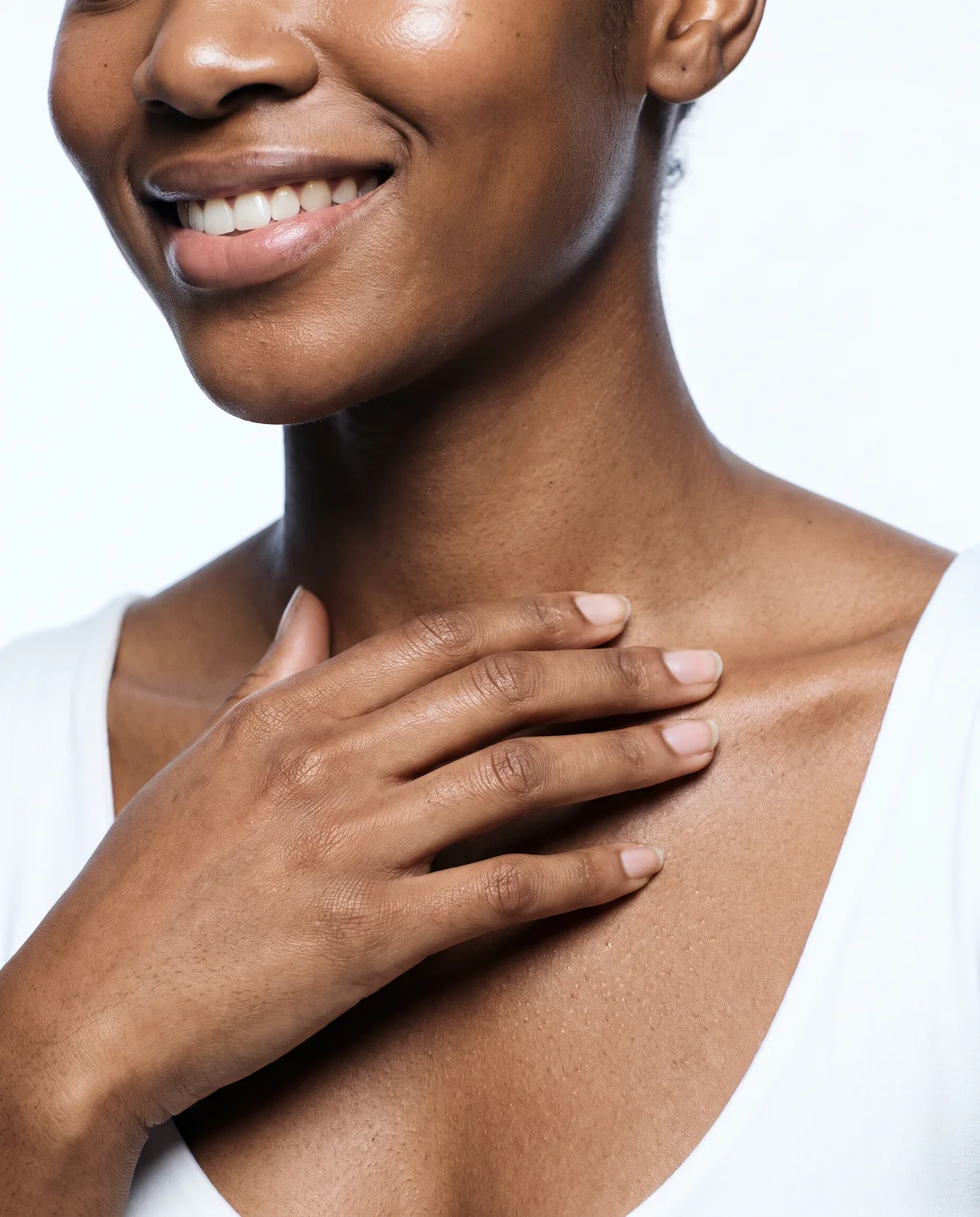 Woman's hand resting on her collarbone, smiling, white background