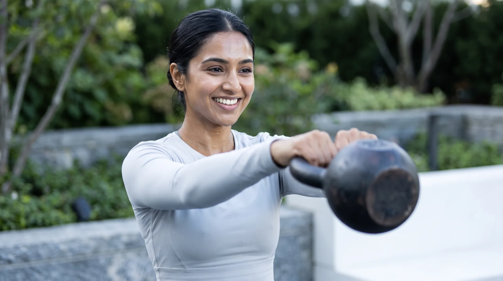 A woman swinging a kettlebell outdoors on a bright morning