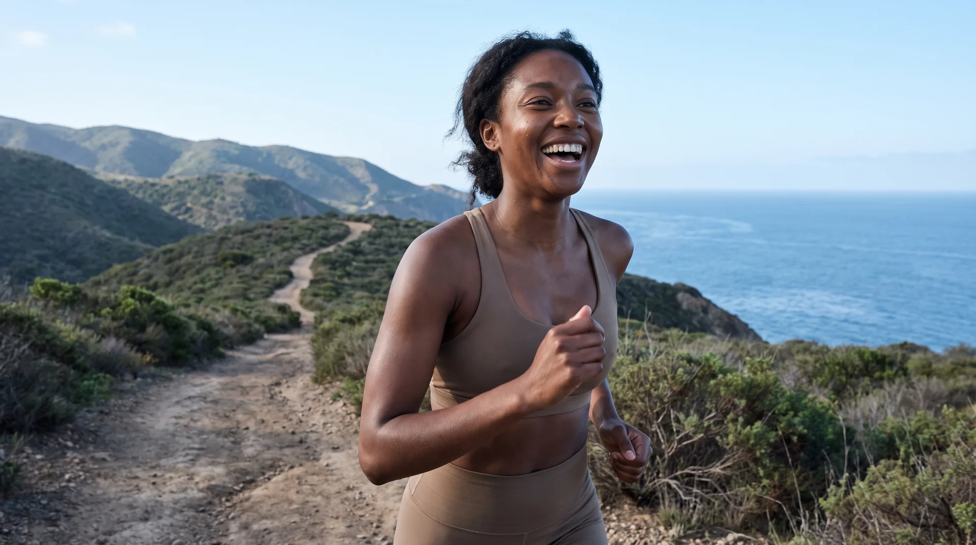 Woman running on a coastal trail at sunrise, smiling