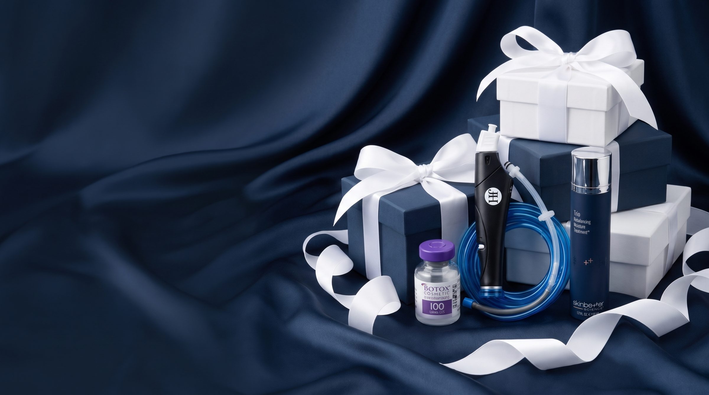 Botox vial, HydraFacial handpiece and SkinBetter skincare with BHRC gift boxes on navy satin